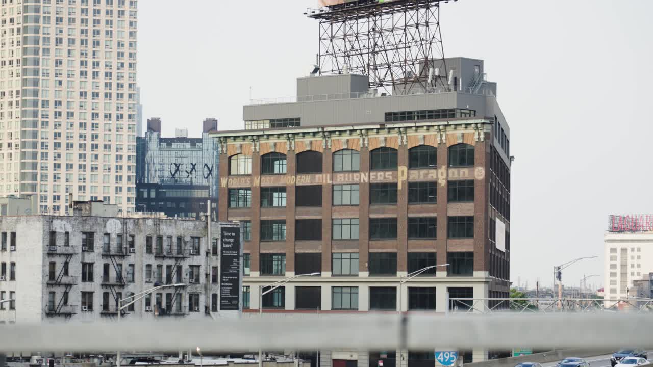 Speeding cars streak past an imposing brown brick warehouse in Queens, New York, their swift motion contrasting the building's solidity
