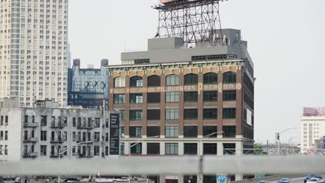 Speeding cars streak past an imposing brown brick warehouse in Queens, New York, their swift motion contrasting the building&#039;s solidity