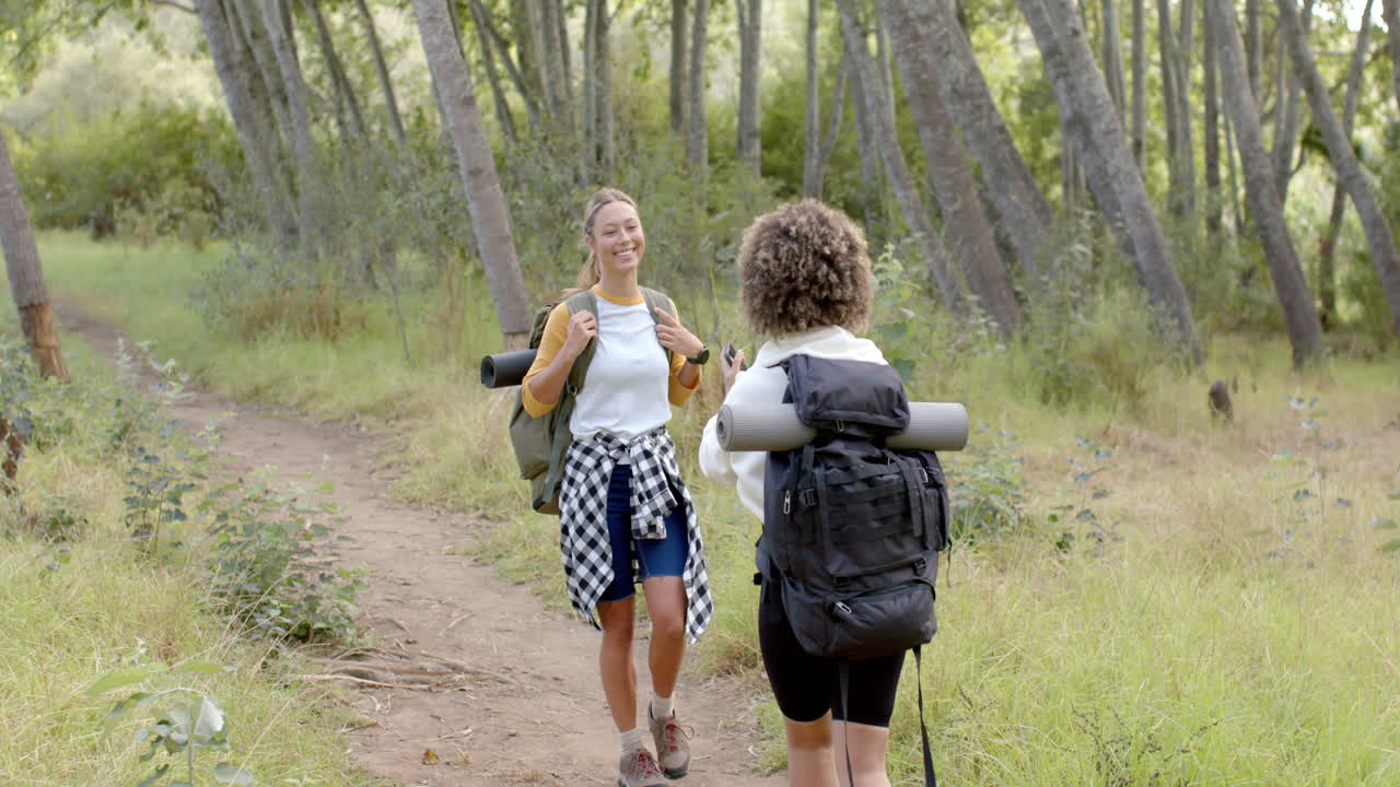 dos mujeres están caminando por un sendero forestal, una con una camisa a cuadros atada alrededor de su cintura