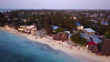 Amazing-Drone-Aerial-Pullback-of-People-Enjoying-Tropical-Tourist-Destination-Nungwi-Beach-During-Sunset,-Zanzibar,-Island-in-Tanzania