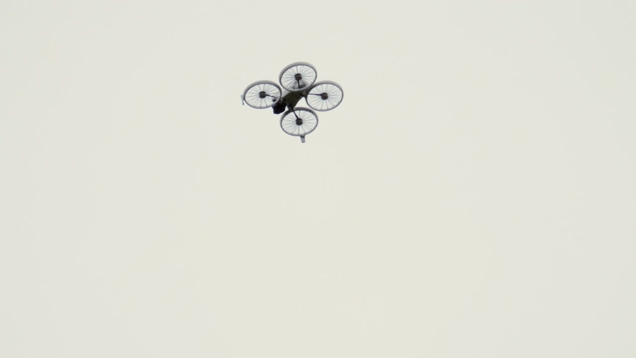 En drönare som flyger högt på en klar himmel, fotograferad underifrån mot en minimalistisk bakgrund