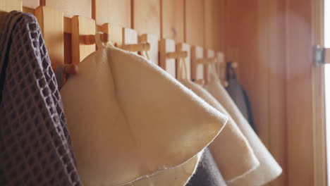 close up of wool sun hats and towels neatly hung on wooden hooks, warm light casting gentle tones on surfaces, with single dry leaf resting on one cap, evoking calm rustic indoor atmosphere