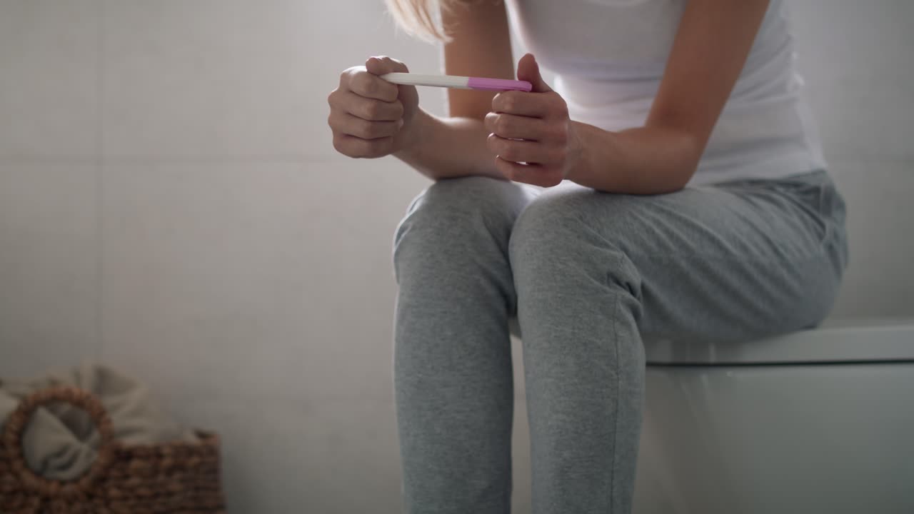 Mujer estresada e irreconocible sentada en el inodoro esperando los resultados de la prueba de embarazo