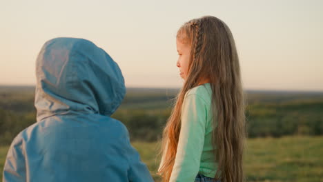 friendly children enjoy sun shower in sunset field boy in raincoat holds elder sister hand walking