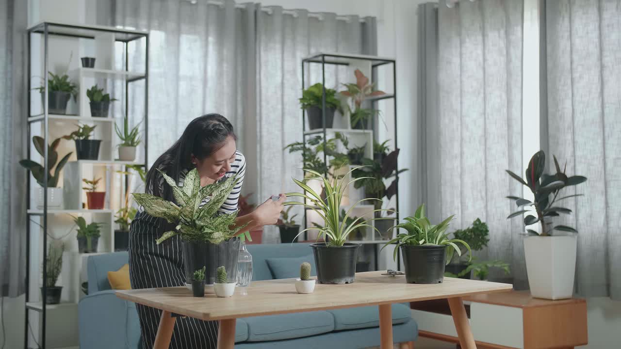 Wanita Asia Tersenyum Memegang Smartphone dan Mengambil Foto Tanaman di Rumah