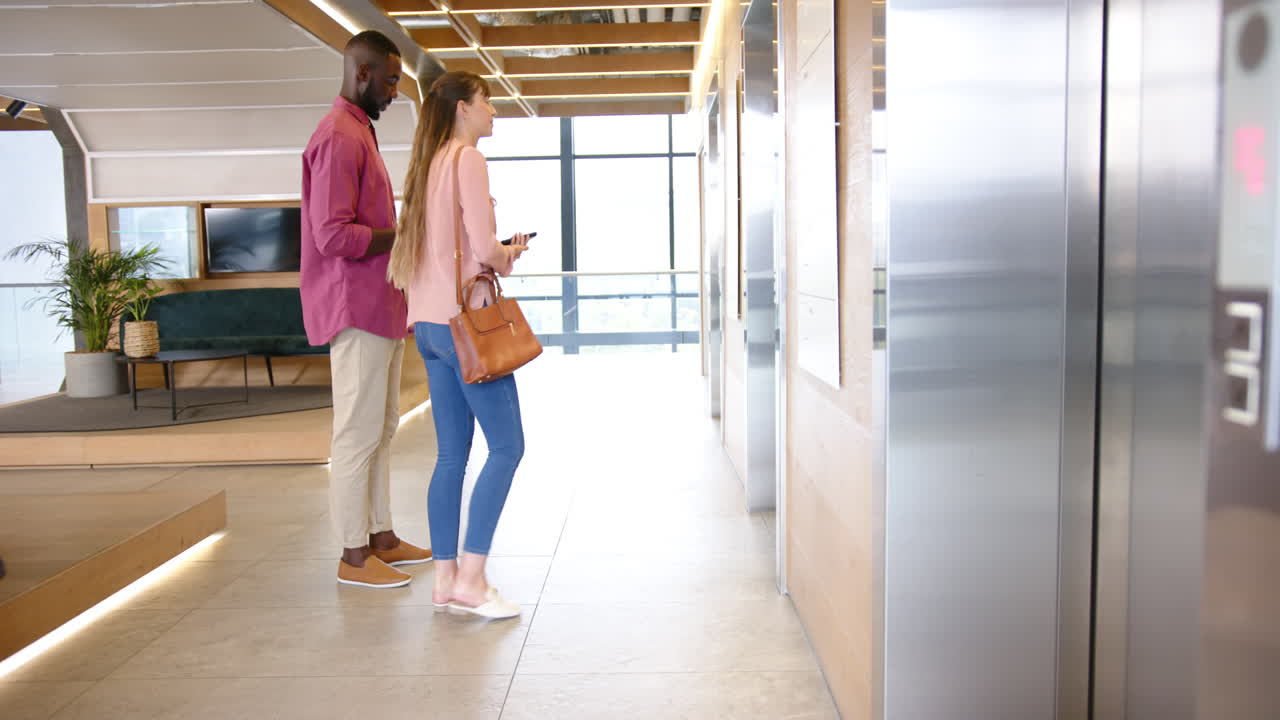 Waiting for elevator, business diverse colleagues holding smartphones in modern office lobby