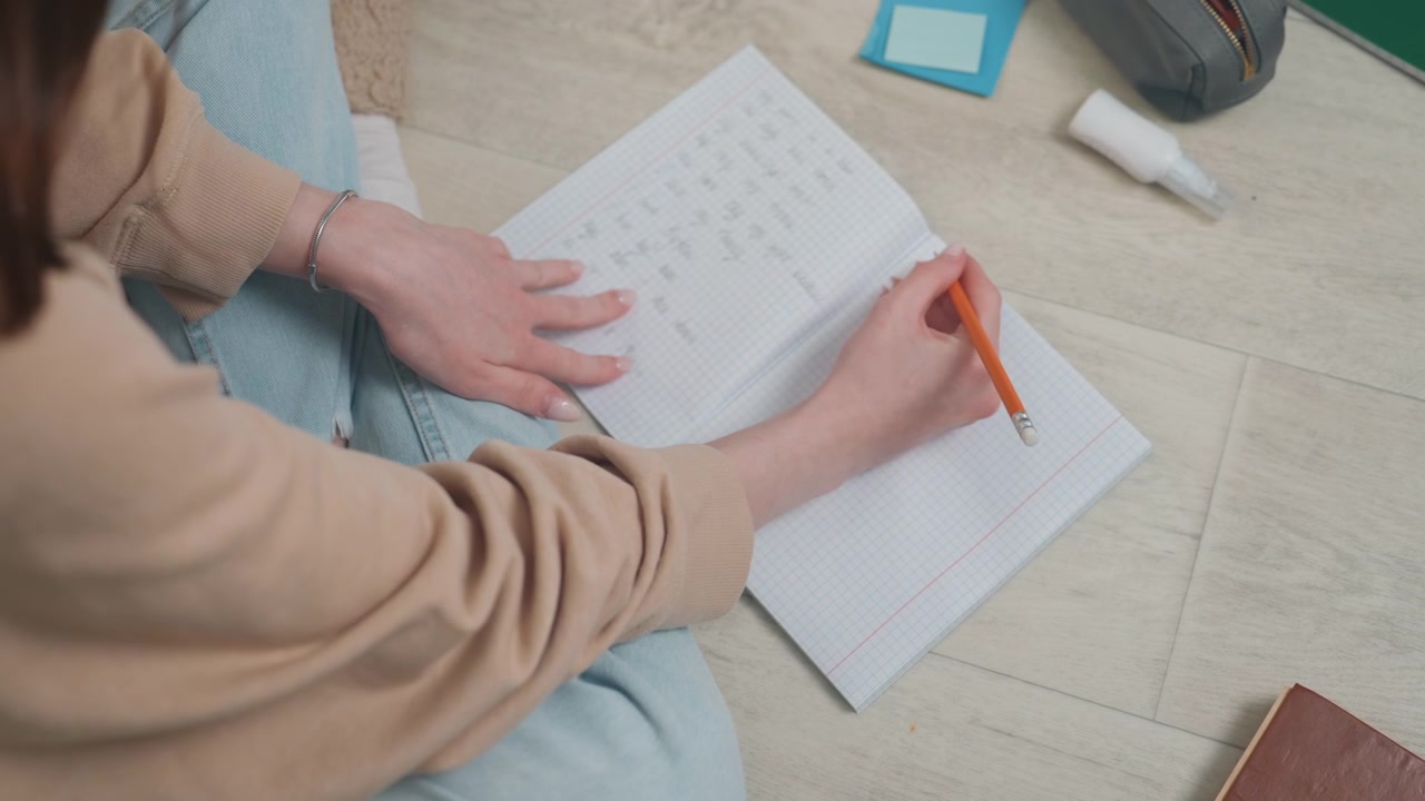 Studente che completa un quaderno di esercizi di grammatica sul pavimento, tratti di matita costanti, prendere appunti con attenzione, maglione casual, astuccio per la cancelleria organizzato, concentrazione calma e progressi costanti durante la pratica individuale.