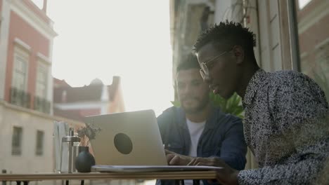 multiethnic freelancers using laptop and talking in outdoor cafe