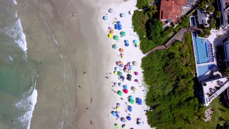 aerial top down view of bombinhas beach with people and umbrellas and a hill on the right