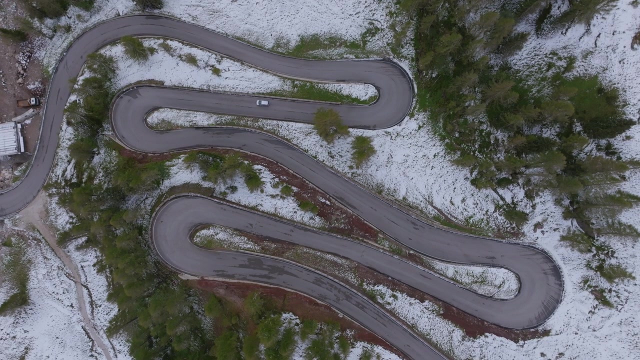 Static aerial top down footage of a winding mountain road in the snow by the town of San Martino di Castrozza, Italy.