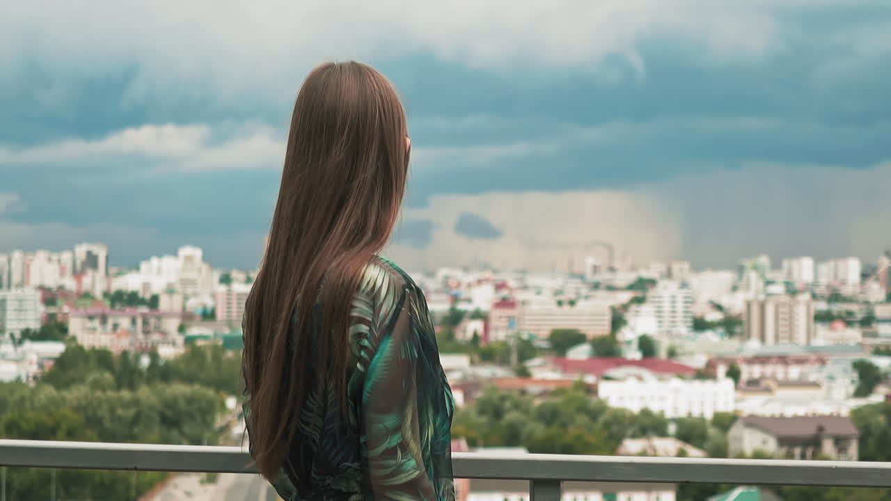 mujer de cabello largo y elegante mira la ciudad desde la cubierta de observación