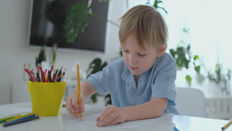 un niño pequeño sentado en la mesa dibuja una pintura con lápiz en diferentes colores