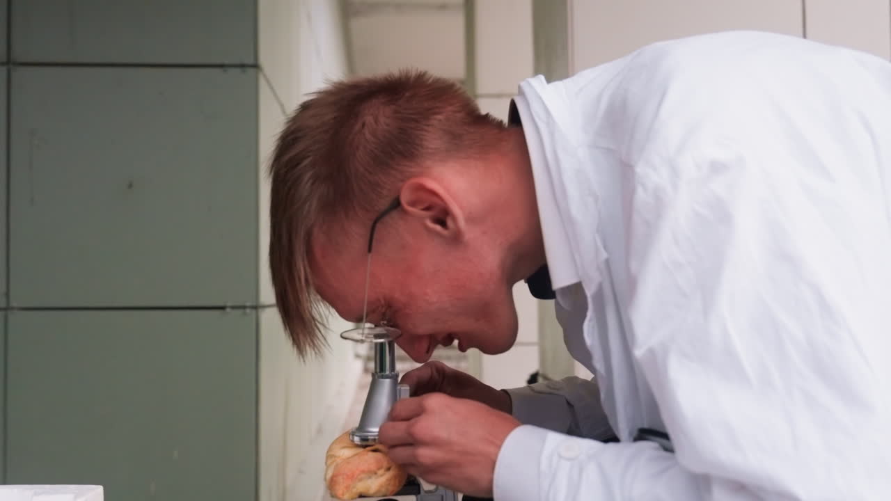 Ecologist in white coat carefully examining pastry closely through microscope in outdoor setting, reflecting curiosity, focus, and scientific observation while jotting with pen during detailed study
