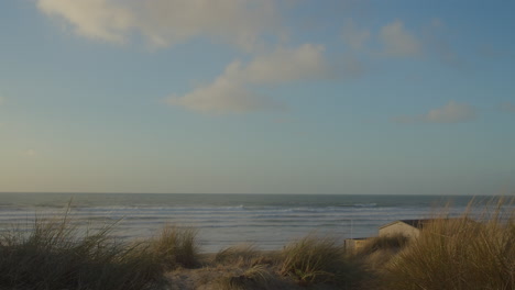 a house behind dunes on windy coast, perran sands beach, golden light