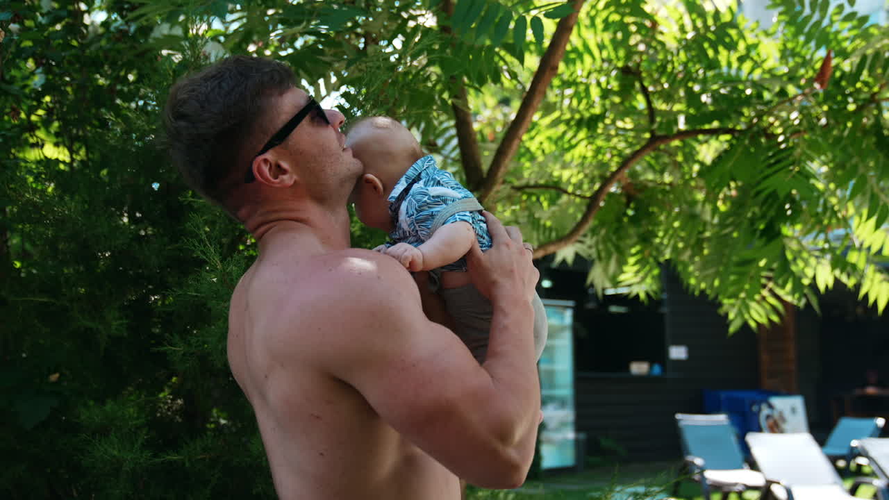 Strong Caucasian man with naked torso holding a baby on one hand above the head. Father is playing with an infant son.