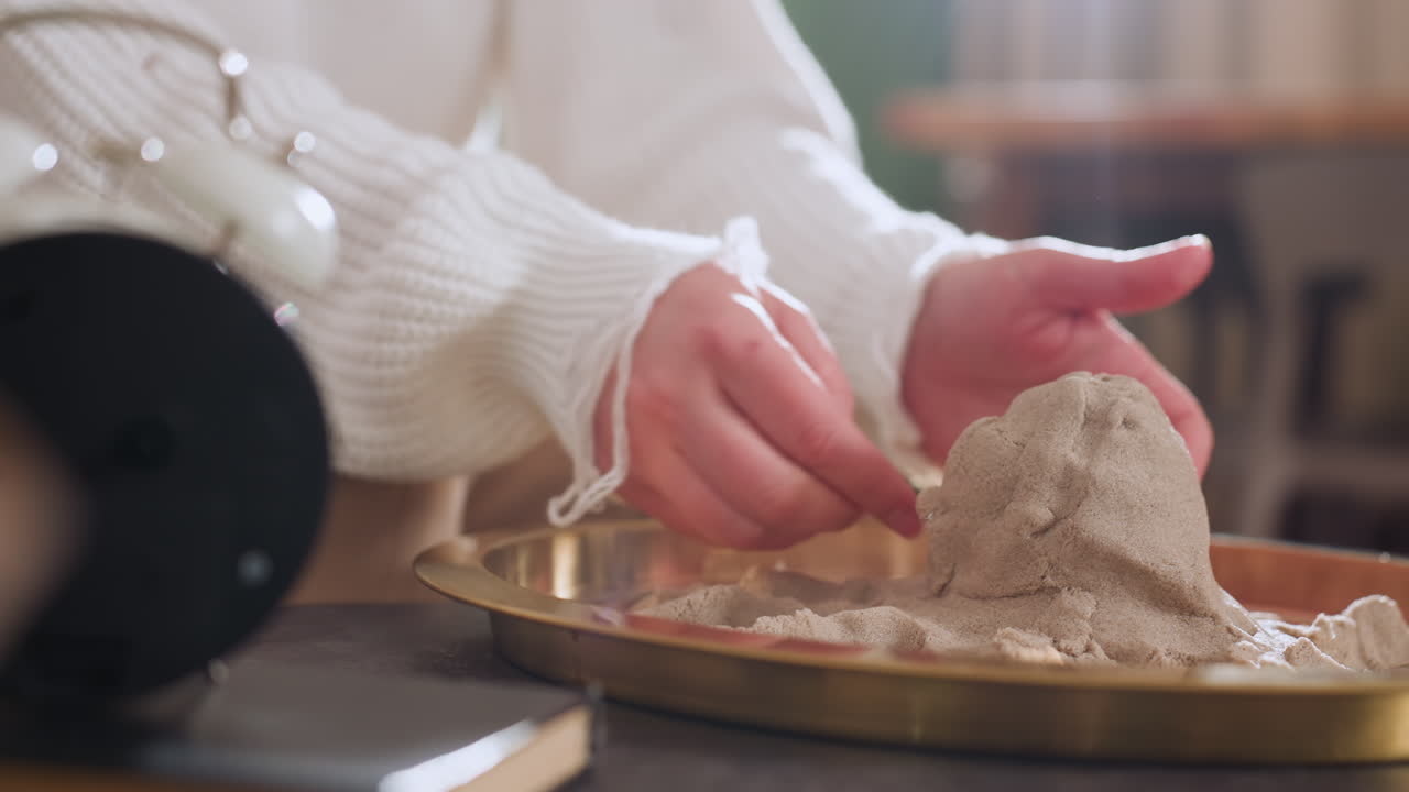 Hand view of explorer shaping octopus from soft moldable material in tray during therapy session, highlighting mindful sculpting process and delicate hand positioning in warm indoor setting