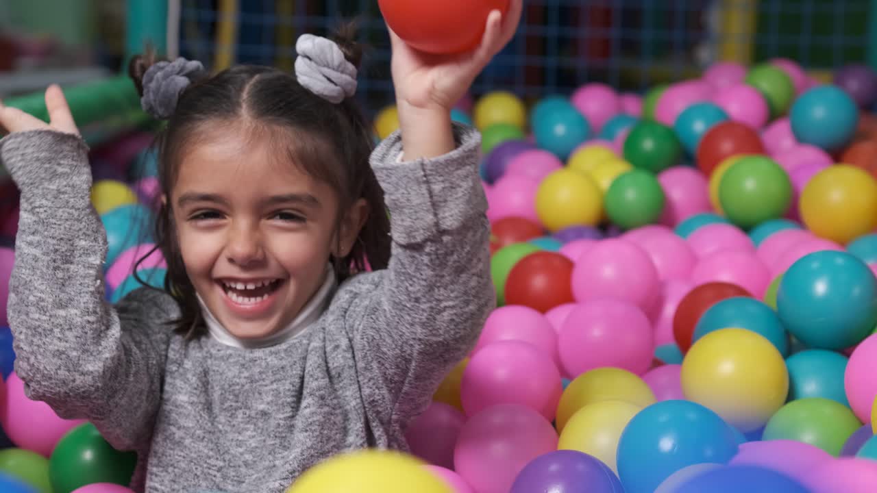 Menina feliz em uma piscina de bolinhas jogando bolinhas para a câmera