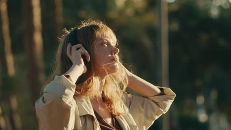 Caucasian-woman-holds-headphones-while-listening-to-music-in-nature-at-sunset