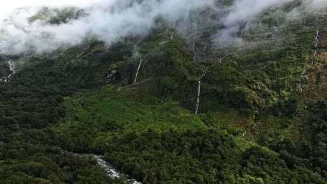 Waterfalls-cascade-along-every-cliff-edge-dropping-into-river-below-clouds-floating-in-air