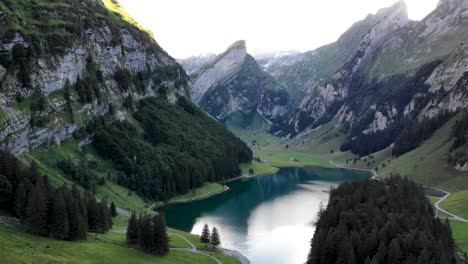 Aerial-flyover-up-alongside-the-shores-of-lake-Seealpsee-in-Appenzell,-Switzerland-with-a-reflection-of-the-Alpstein-peaks-on-the-lake's-water