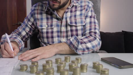 close up of man’s hands counting coins doing accounting and writes down numbers on a paper