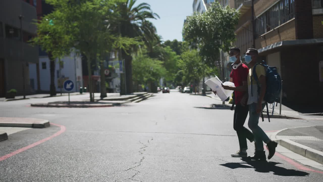 Dois amigos multirraciais usando máscaras faciais, caminhando e usando um mapa na rua.