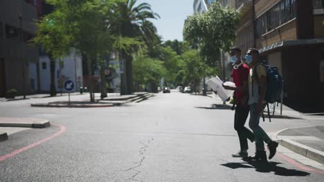 Two-mixed-race-male-friends-wearing-face-masks,-walking,-using-map-in-the-street