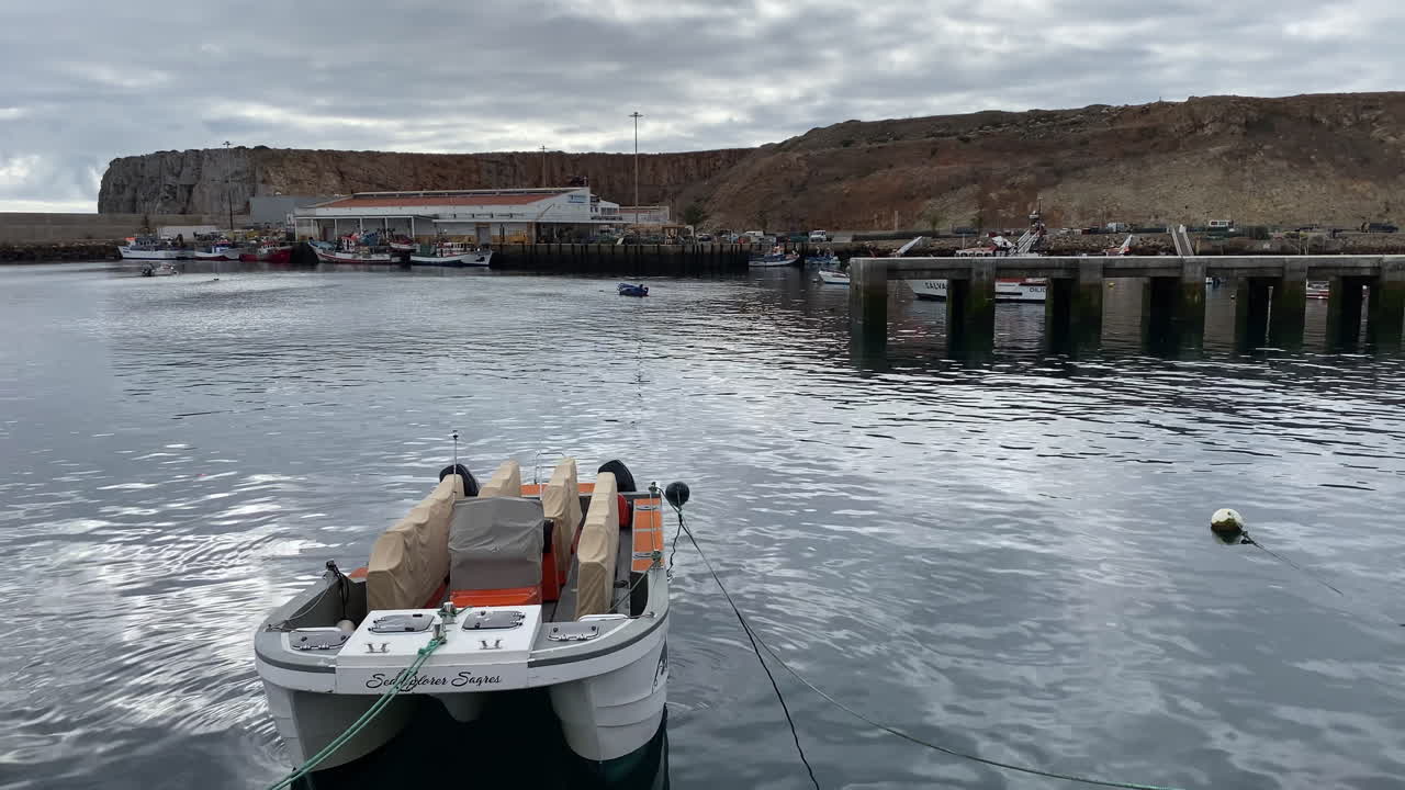 A weathered fishing boat floats quietly in the turquoise harbor of Sagres under soft morning light