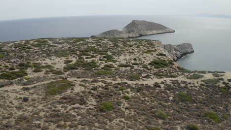 couple on quad bike, atv off-roading on rough rocky road track near sea on ios, greece drone aerial shot