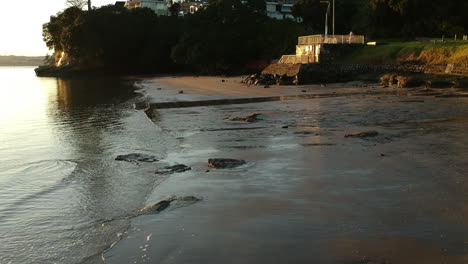 Drone-flies-over-small-waves-along-the-shore-of-the-beach-at-sunrise-golden-hour