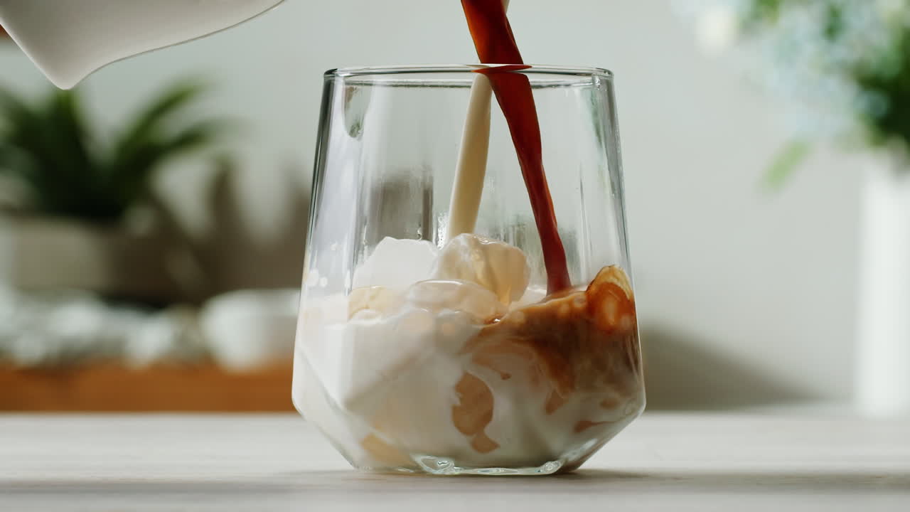 Ice coffee latte with cream being poured into it showing the texture and refreshing look of the drink, with a clean background. High quality 4k footage