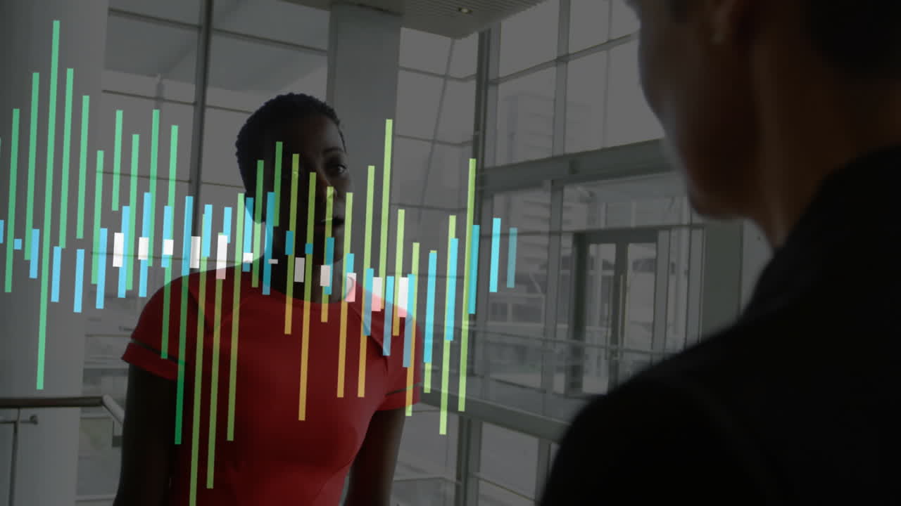 Two colleagues standing in glass atrium, analyzing business trends with holographic bar chart