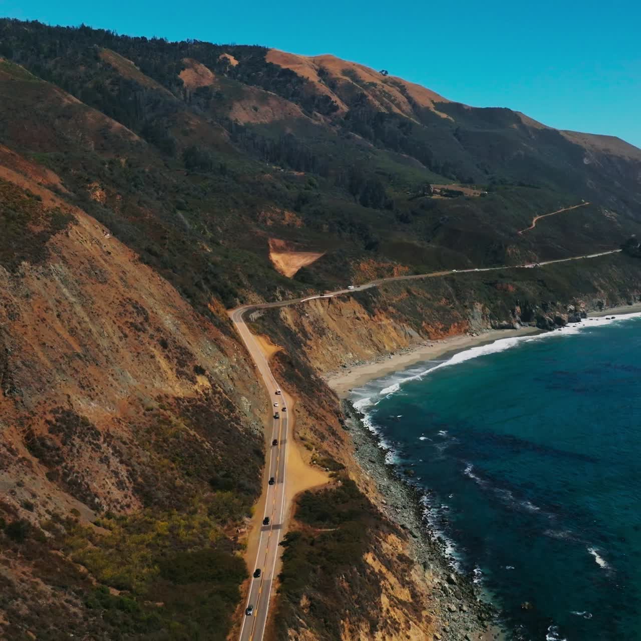 Cars going quickly by the dangerous highway on the rocks of California. Great scenery of beautiful mountains watered by Pacific Ocean waters