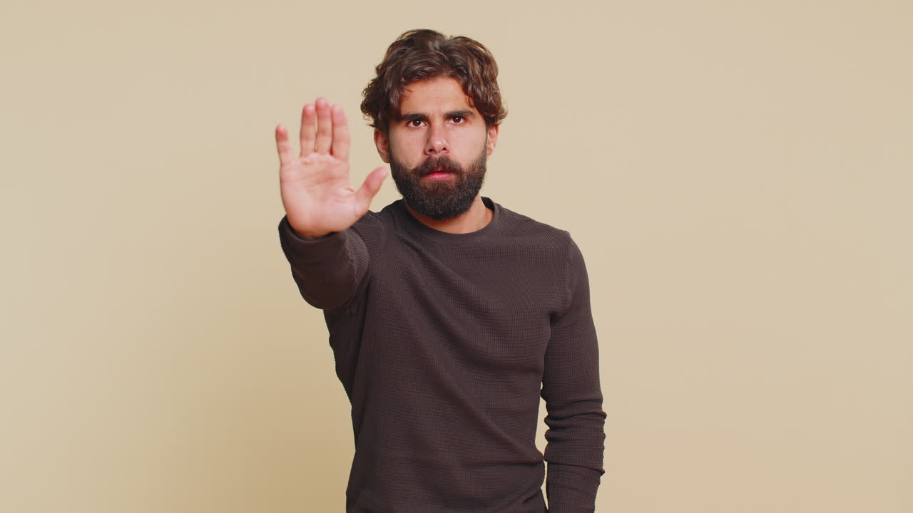 Hindu man says no hold palm in stop gesture warning of finish prohibited access on beige background