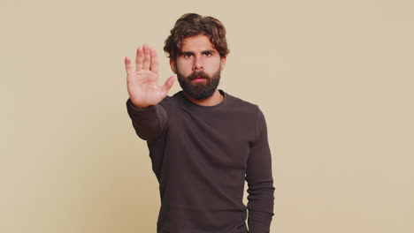 hindu man says no hold palm in stop gesture warning of finish prohibited access on beige background