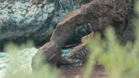 Grass-foreground-out-of-focus-with-small-rock-arch-and-slow-motion-ocean-waves-crashing-on-cliffs