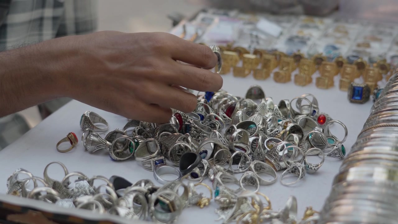 Die Hand eines Kunden durchsucht eine große Sammlung von Silber- und Edelsteinringen auf einem traditionellen Straßenmarkt in Kolkata, Indien. Ideal für Reise-, Kultur- und Einzelhandelsinhalte.