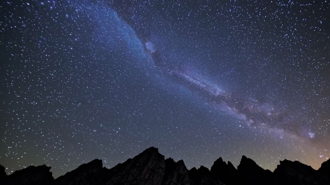 A breathtaking wide-angle shot captures the Milky Way over jagged mountain peaks