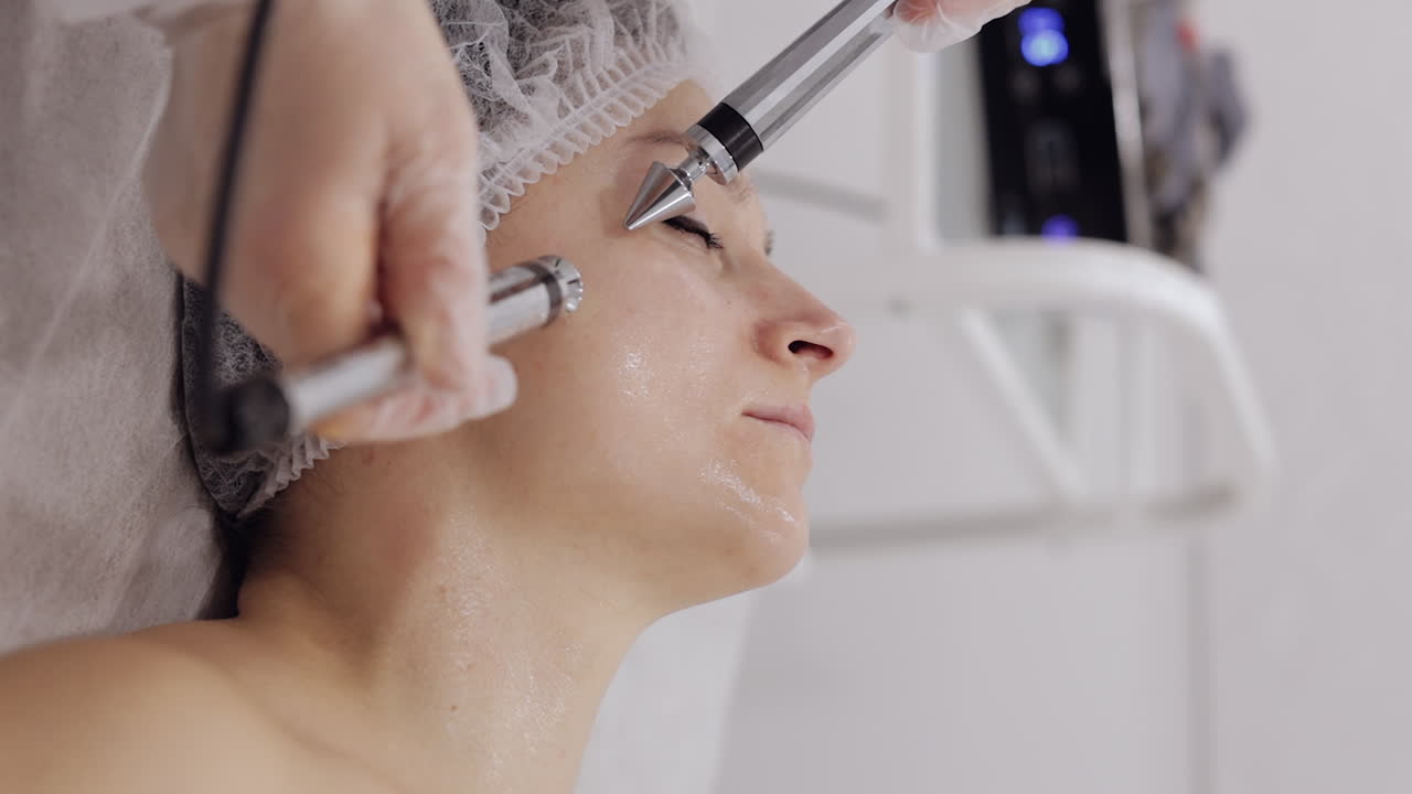 Donna di mezza età che riceve un trattamento viso a microcorrenti per le guance da un'estetista in un salone spa