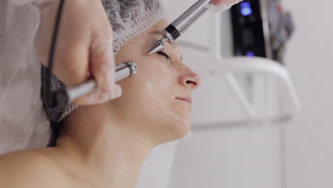 middleaged woman receiving micro currents facial cheek skin treatment from beautician in spa salon