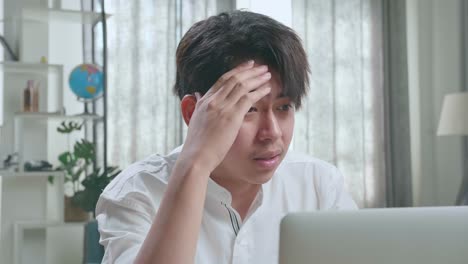close up of asian man student being tired while using computer to study online at home