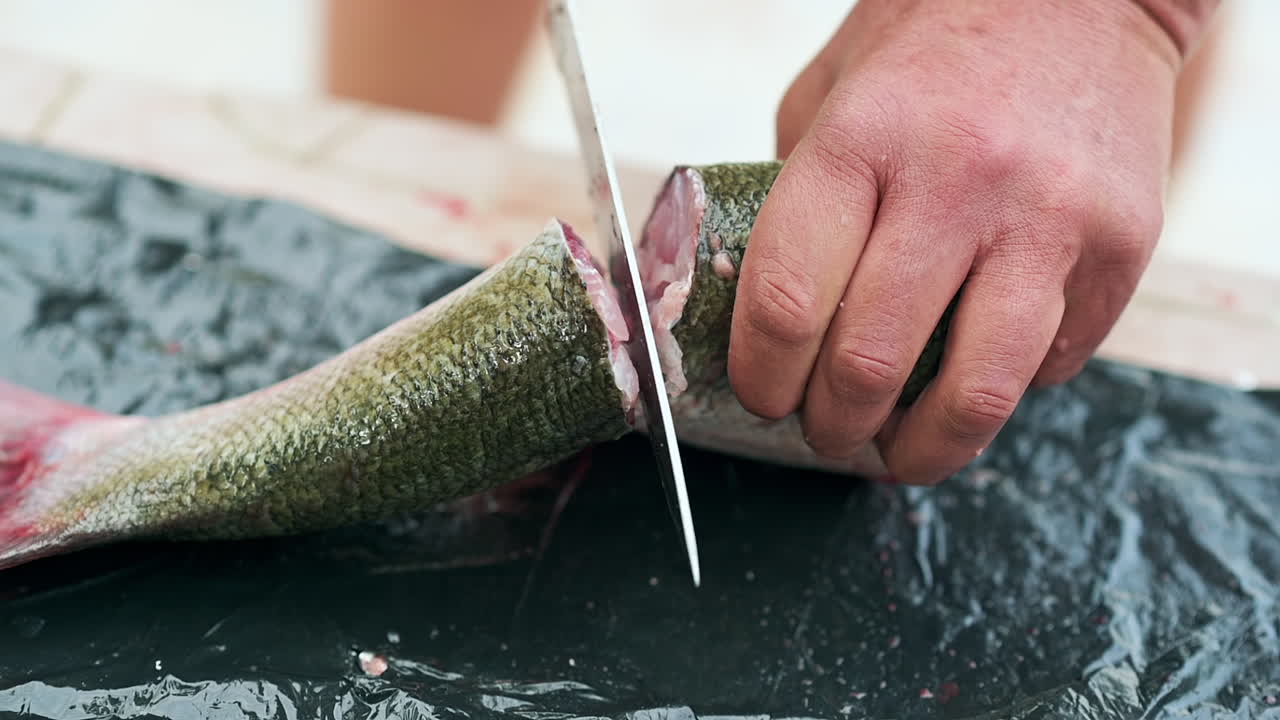 Close up of hands cutting a fish tail on a black surface with a knife