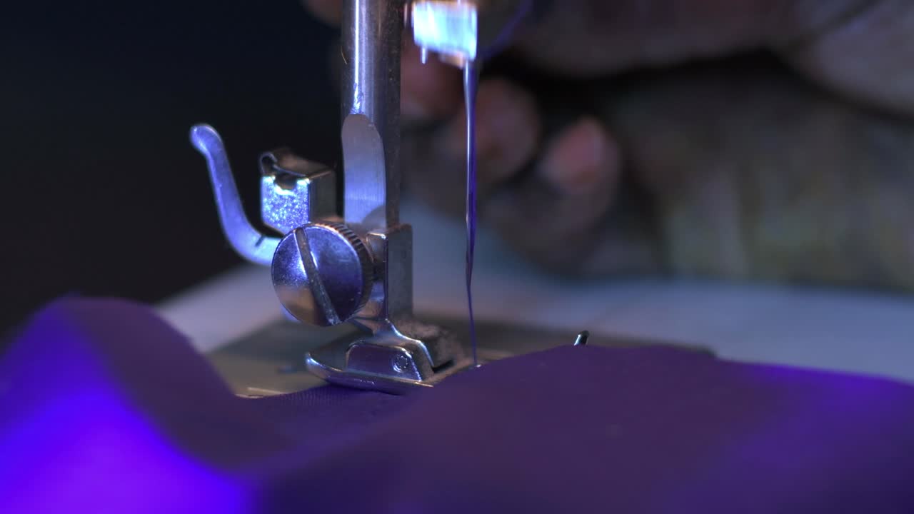 primer plano de una aguja de máquina de coser cosiendo un paño violeta con hilo violeta