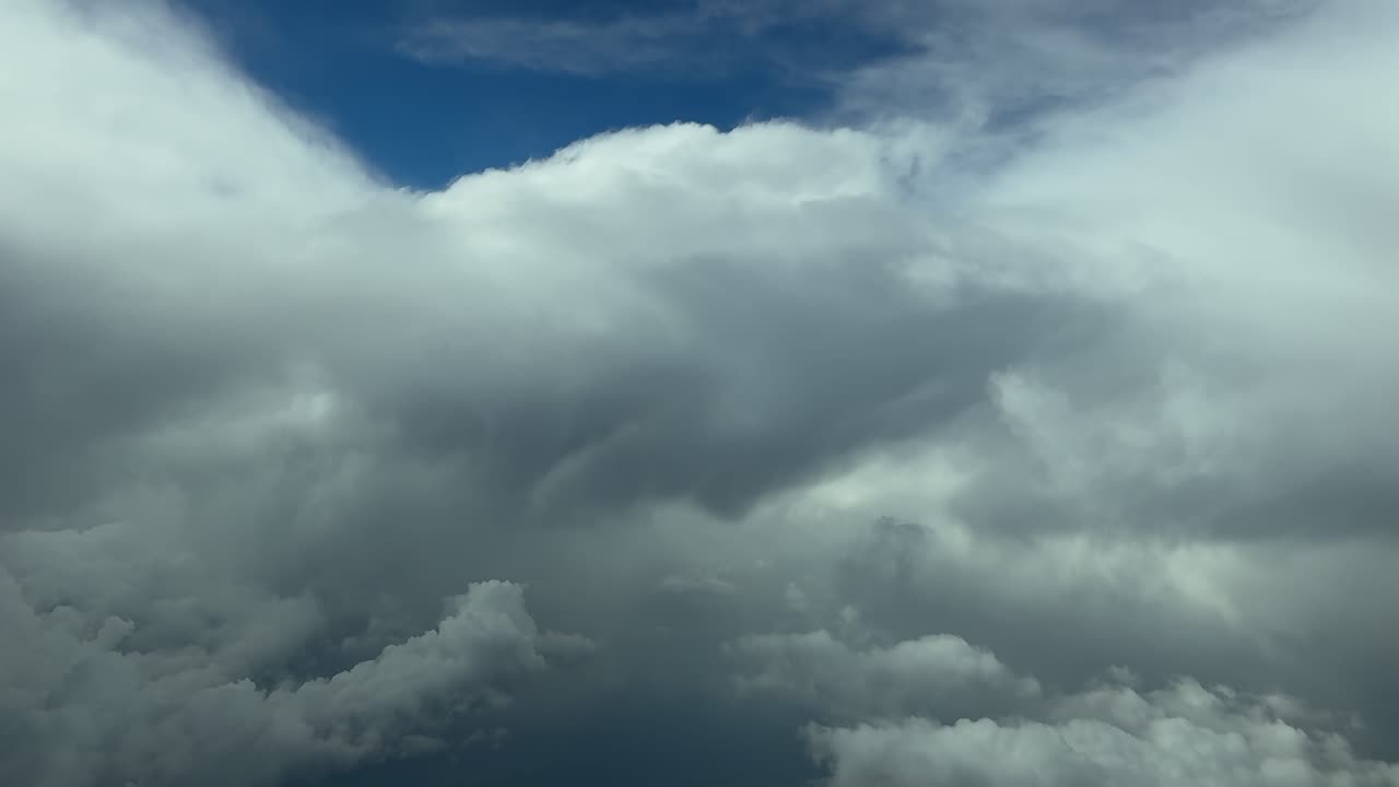 An aerial stormy cloudscape taken from a jet airplane flying toward layers of threatening storm clouds under a deep blue sky.