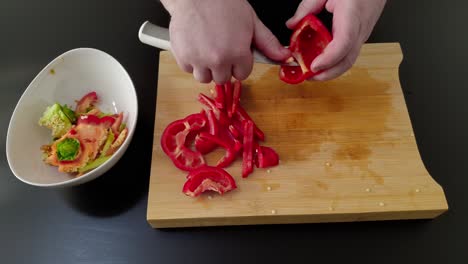 slicing a red bell pepper on a cutting board, medium shot overhead