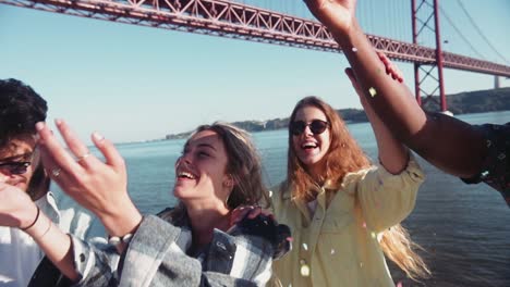 close up multi-ethnic young friends throwing colorful confetti by riverside