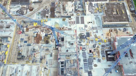 vista aérea de pájaro de un sitio de construcción construyendo grúas mirando hacia abajo área de maquinaria industrial alrededor de apartamentos urbanos residenciales