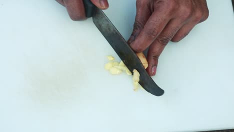 peeled ginger is cut into small pieces using a knife on a shopping board ,traditional outdoor cooking