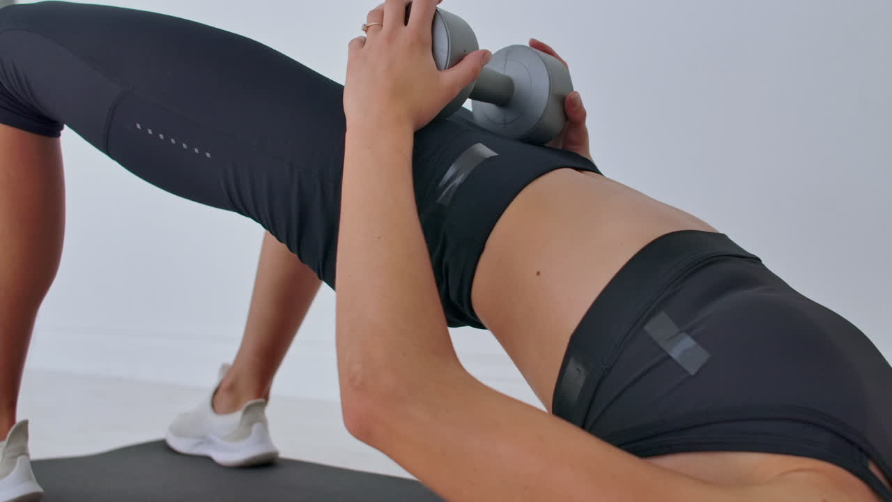 Portrait of young motivated athletic female making pelvis lifting with weights indoors