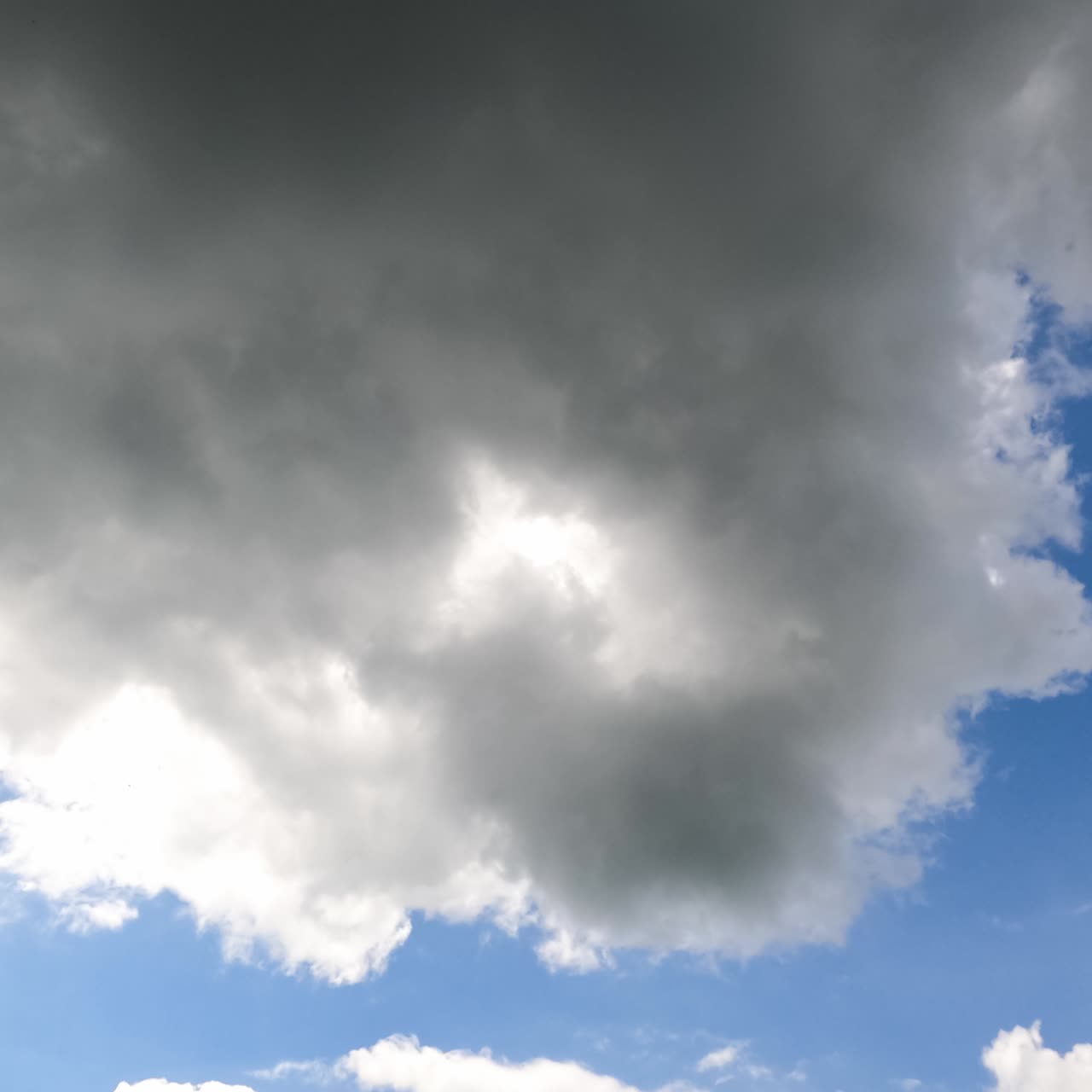 White and grey clouds forming in the blue sky. Rays of sun breaking through the clouds timelapse. View from below